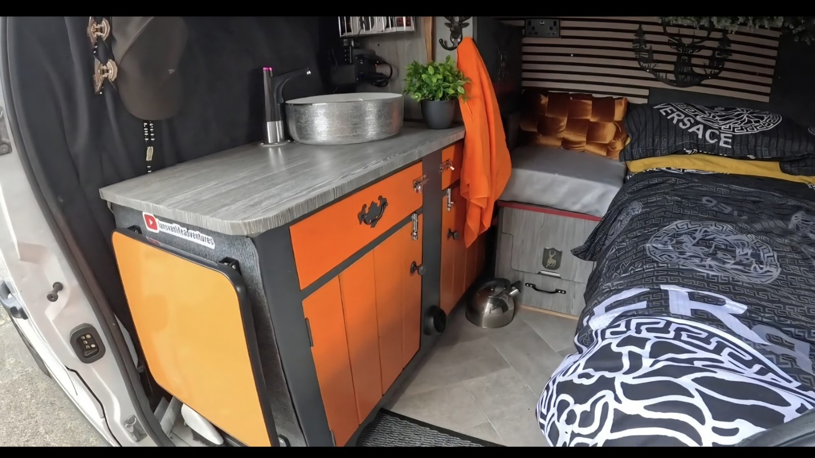 The real interior of Ian's campervan with orange and black kitchen units and sleeping area